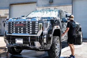 Man washing a black GMC truck covered in soap foam