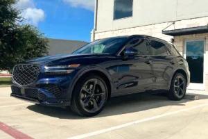 Side view of blue Genesis GV70 SUV parked in front of a building