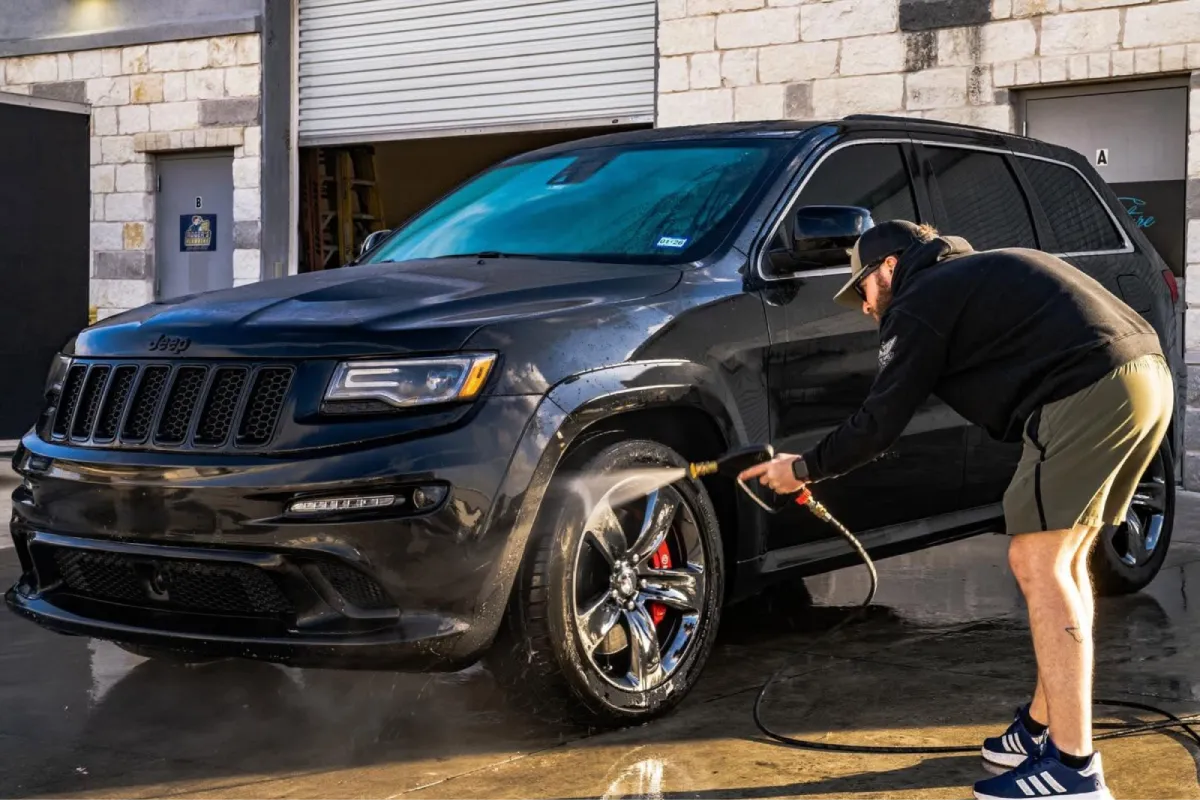 Car detailing technician pressure washing black SUV