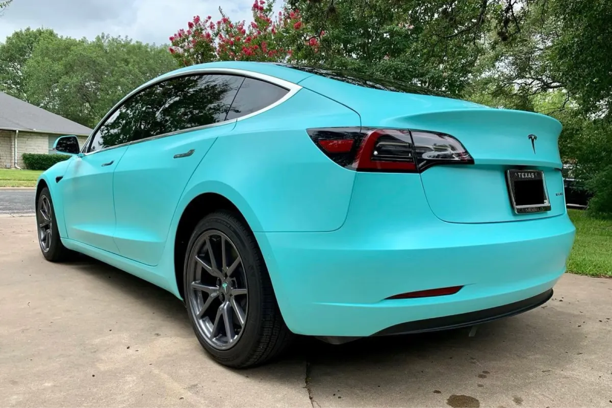 Rear side view of a Tesla with a turquoise vinyl wrap.